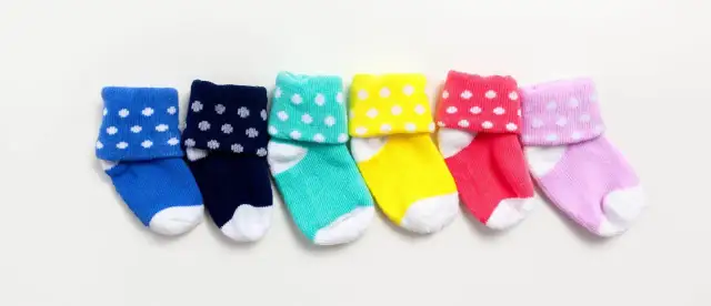 Sześć kolorowych skarpetek niemowlęcych w białe kropki, ułożonych obok siebie na białym tle.