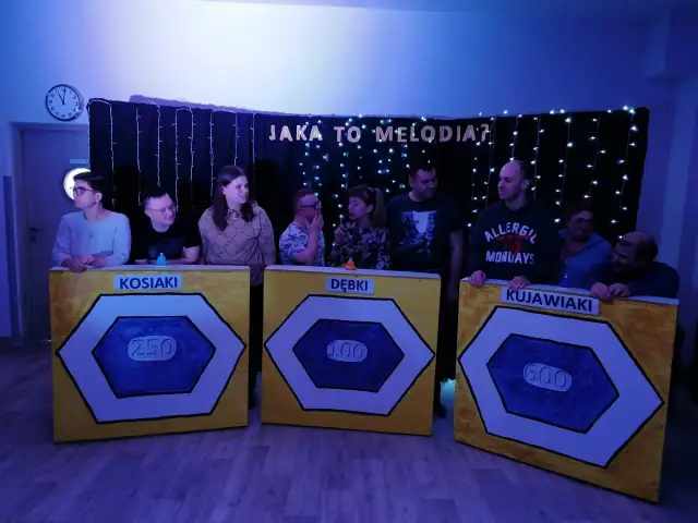 Uczestnicy zabawy "Jaka to melodia?" stoją przy planszach z nazwami drużyn: Kosiaki, Dębki, Kujawiaki.