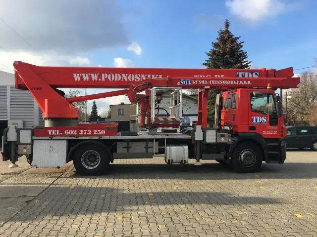 Czerwony podnośnik koszowy WUMAG WT 450 z koszem roboczym i wysięgnikiem. Na pojeździe widnieje napis WWW.PODNOSNIKI-TDS.PL.