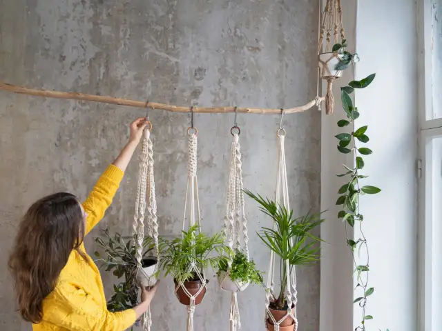 Kobieta w żółtym swetrze wiesza rośliny w doniczkach na ozdobnych sznurkach. To piękny przykład, jak można stworzyć własne dekoracje diy makrama.