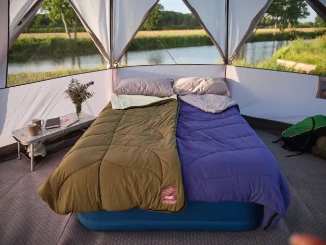 Dwa śpiwory, zielony i fioletowy, leżą na dmuchanym materacu w namiocie. To inspiracja, jaki śpiwór wybrać na kemping nad jeziorem.