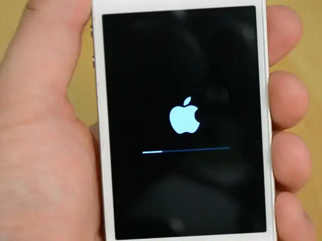 Dłoń trzyma biały iPhone z logo Apple i paskiem postępu. To ekran, który pojawia się, gdy próbujesz jak zresetować iPhone.