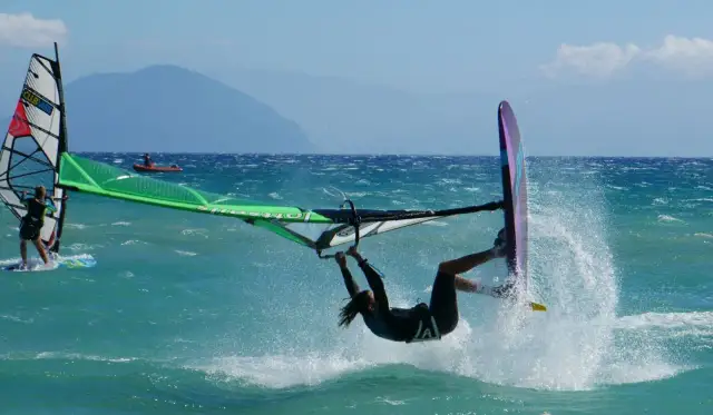 Windsurfer wykonuje akrobację na turkusowej wodzie, tworząc fontannę rozprysków.