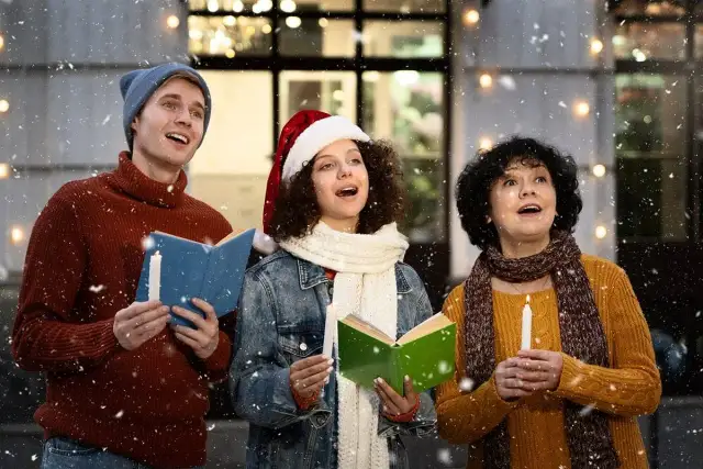 Trzy osoby śpiewają kolędy, trzymając świece i książeczki z tekstem "Rokiczanka Pastorałka od serca do ucha".