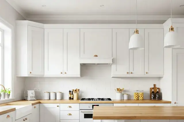 Nowoczesna biała kuchnia z drewnianym blatem i złotymi uchwytami.