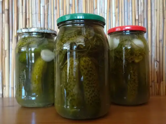 Trzy słoiki z ogórkami kiszonymi, na tle bambusowej maty.