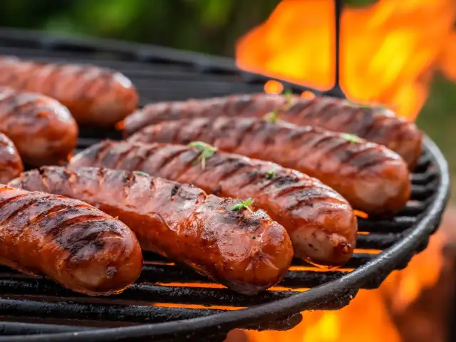 Kiełbaski śląskie grillowane na ruszcie z płomieniami w tle.