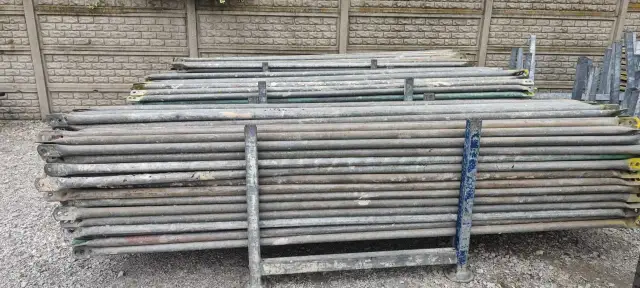 Stos rusztowań Plettac na tle betonowego muru.