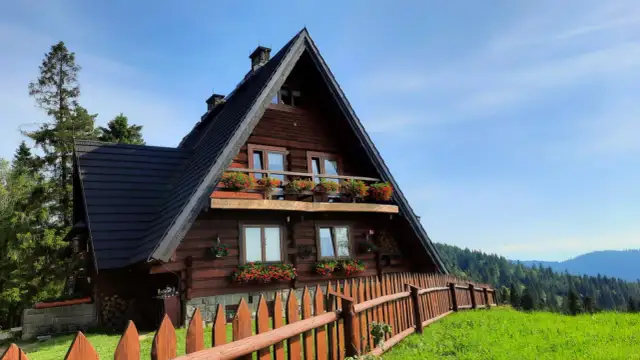 Drewniana bacówka na Maciejowej, otoczona zielenią i drewnianym płotem, z balkonem pełnym kwiatów.