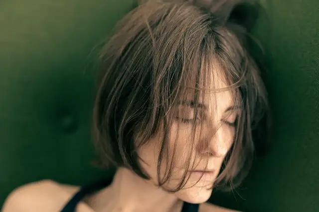 Kobieta z zamkniętymi oczami, włosy opadające na twarz, na zielonym tle.