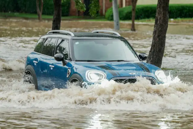 Niebieski Mini Cooper przedziera się przez powódź. Ubezpieczenie GAP przy zakupie za gotówkę chroni przed stratami w takich sytuacjach.