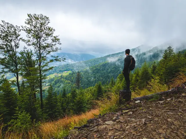 Mężczyzna z plecakiem podziwia widok na górzyste, zalesione tereny. To prawdziwy hiking po polsku, z mgłą unoszącą się nad dolinami.
