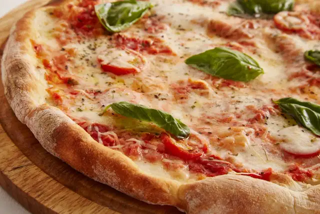 Zbliżenie na świeżo upieczoną pizzę z pomidorami, mozzarellą i bazylią na drewnianej desce.