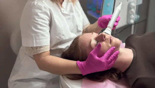 Zabieg oczyszczania wodorowego. Kosmetolog w różowych rękawiczkach wykonuje zabieg na twarzy klientki. Brak widocznych skutków ubocznych.