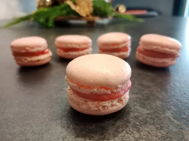 Kilka różowych makaroników z kremowym nadzieniem na ciemnym blacie.