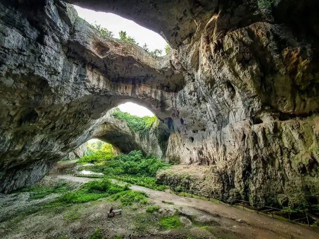 Wielkie skalne mosty w jaskini, przez które widać bujną zieleń. Niezwykłe krajobrazy gór Bałkan.