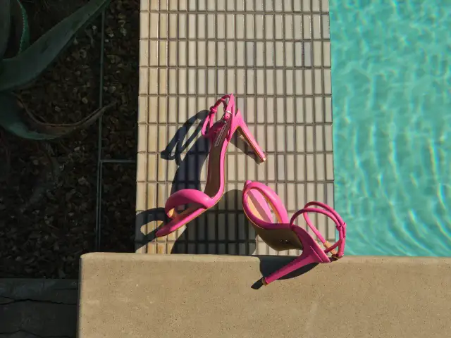 Różowe sandały na obcasie leżące na krawędzi basenu.