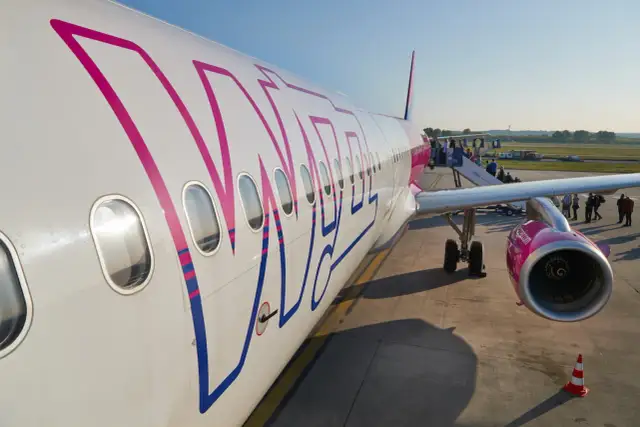 Samolot Wizz Air z widocznym logo, pasażerowie wsiadają po schodkach.