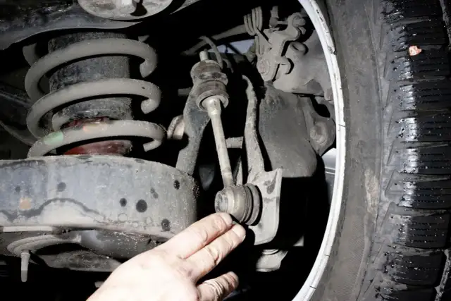 Dłoń wskazuje na łącznik stabilizatora, który odpowiada za stabilność pojazdu podczas pokonywania zakrętów.