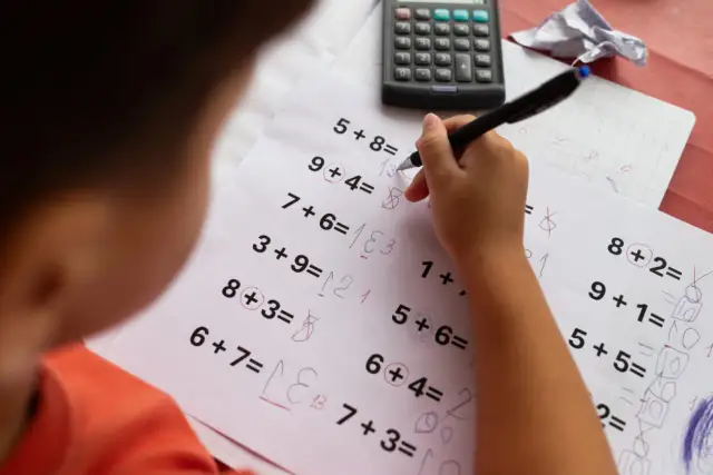 Dziecko rozwiązuje zadania matematyczne, próbując pokonać dyskalkulię. Widoczny kalkulator i zeszyt sugerują naukę.