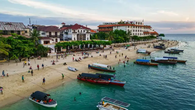Tanzański szyling na plaży w Stone Town, Zanzibarze. Ludzie odpoczywają, bawią się i pływają, a łodzie czekają na turystów.