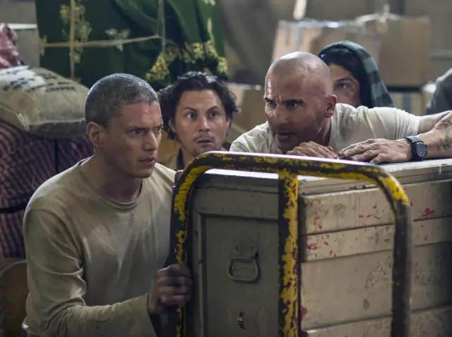 Dwóch mężczyzn, jeden skazany na śmierć, spogląda z napięciem na coś za skrzynią.