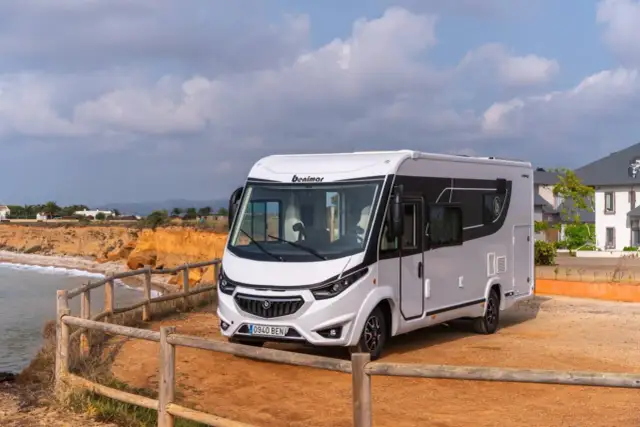 Biały kamper Benimar zaparkowany na żwirowym placu przy klifie nad morzem.