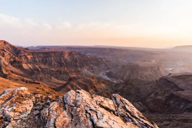 Wąwóz Fish River w Namibii, z rzeką wijącą się w dole. Zachodzące słońce maluje skały na ciepłe barwy.
