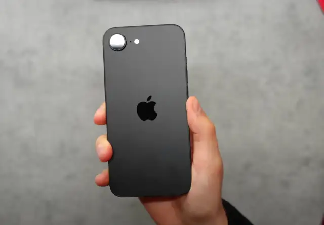 Czarna obudowa iPhone SE 4 z charakterystycznym jabłkiem Apple. Telefon trzymany w dłoni na szarym tle.