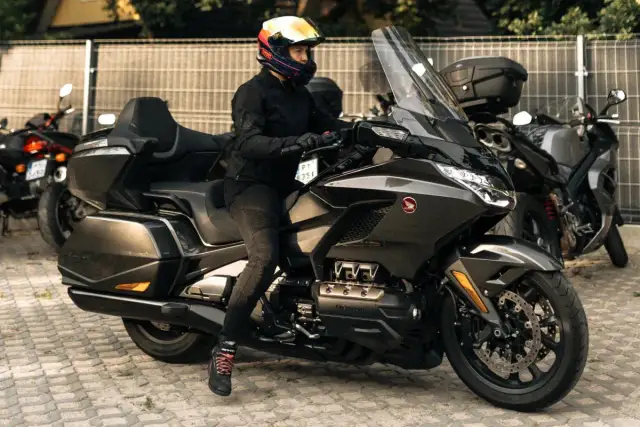 Kobieta w kasku na potężnym motocyklu turystycznym, obok inne rodzaje motocykli.