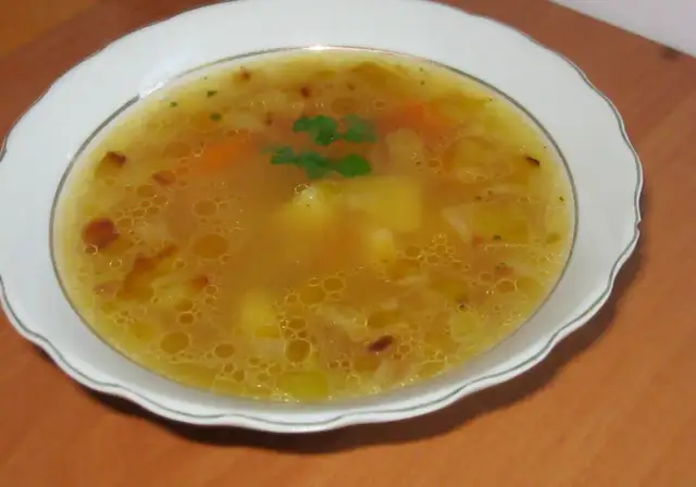 Prosta zupa cebulowa z ziemniakami, z kawałkami marchewki i natką pietruszki, podana w białej misce.