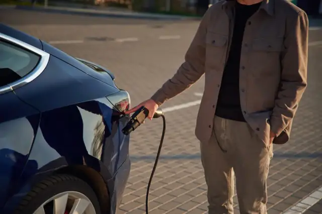 Mężczyzna podłącza ładowarkę do ciemnoniebieskiego samochodu elektrycznego. Zastanawiasz się, ile kosztuje ładowanie samochodu elektrycznego?