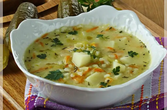 Aksamitna zupa ogórkowa na żeberkach, pełna ziemniaków, marchewki i koperku, z ogórkami w tle.