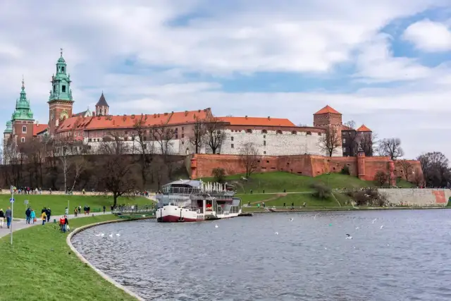 Zamek Królewski na Wawelu nad Wisłą, z łodzią i spacerującymi ludźmi.