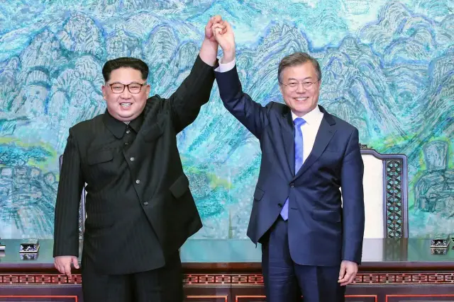 Kim Dzong Un, prezydent Korei Północnej, i Moon Jae-in pozdrawiają publiczność, trzymając się za ręce.