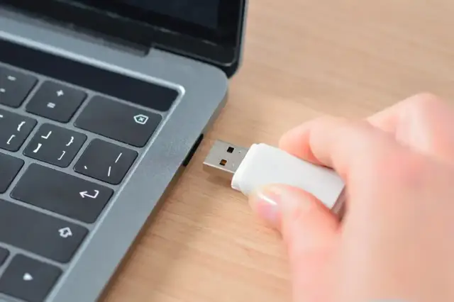 Dłoń wkłada pendrive do laptopa, przygotowując się do zapisania prezentacji Google na pendrive.