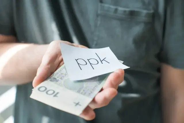 Dłoń trzyma plik banknotów i kartkę z napisem "ppk". Zastanawiasz się, ile można wpłacać na PPK?