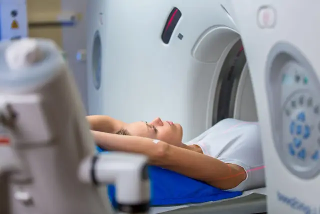 Kobieta leży na łóżku tomografu. Czy do tomografii trzeba się rozbierać? Zazwyczaj nie, wystarczy zdjąć metalowe przedmioty.