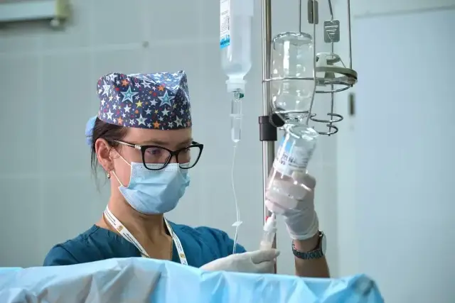 Pielęgniarka w maseczce i czepku z gwiazdkami przygotowuje kroplówkę. Czy pielęgniarka zarobki są adekwatne do jej pracy?