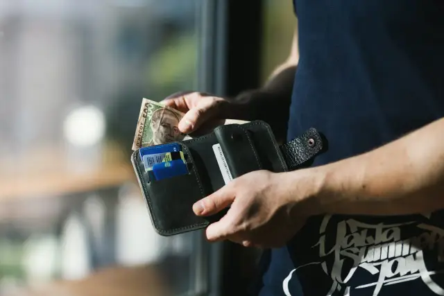 Ręce wkładają banknot 500 hrywien do portfela. Kto płaci pośrednikowi przy sprzedaży mieszkania? Prawdopodobnie sprzedający.