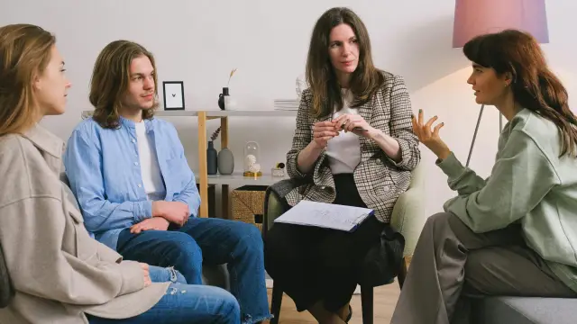 Grupa osób uczestniczy w sesji psychoterapii systemowej. Terapeuta prowadzi rozmowę, słuchając uważnie uczestników.