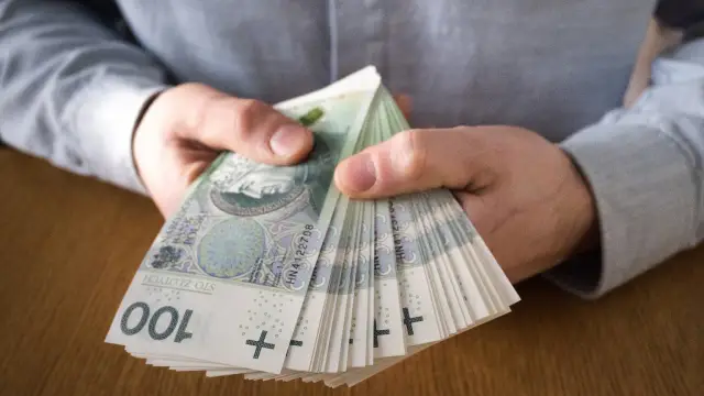 Dłonie trzymające stos banknotów 100 zł. Taka dyspozycja na wypadek śmierci zapewnia spokój bliskim.