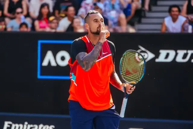 Australijski tenisista Nick Kyrgios z palcem na ustach, trzymający rakietę na korcie.