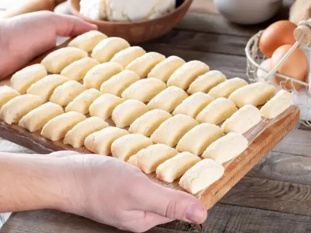 Ania gotuje pierogi leniwe. Na desce leżą rzędy gotowych do gotowania pierogów leniwych, obok jajka i twaróg.