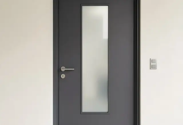 Nowoczesne, szare drzwi zewnętrzne z matową szybą i metalową klamką. Idealne, jakie drzwi zewnętrzne do minimalistycznego domu.