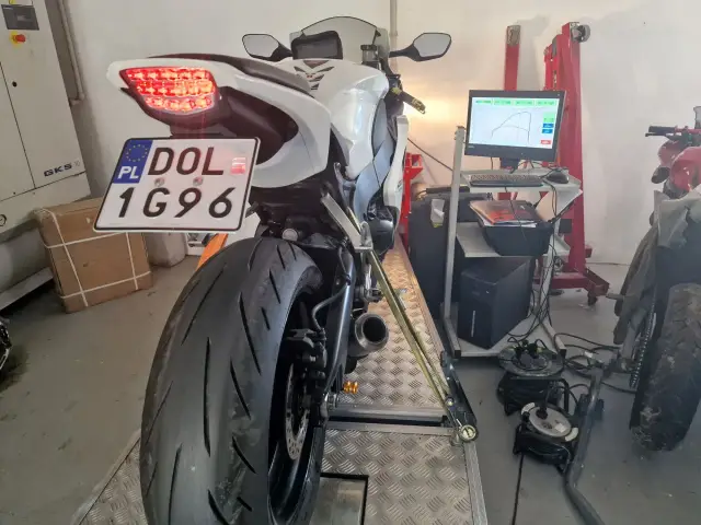 Biały motocykl na hamowni, przygotowany do pomiaru mocy. Widoczna tablica rejestracyjna DOL 1G96. Blokowanie motocykla na A2 to kluczowy etap testów.