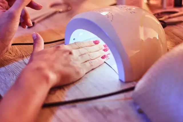 Dłoń z różowymi paznokciami w kropki, utwardzanymi w lampie UV. Efekt bubble nails gotowy!