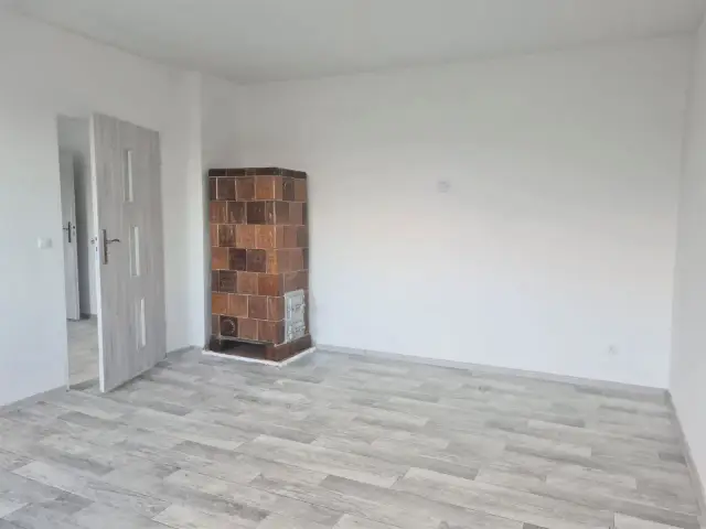 Puste pomieszczenie z piecem kaflowym i drzwiami. To może być przyszłe mieszkanie komunalne po remoncie.