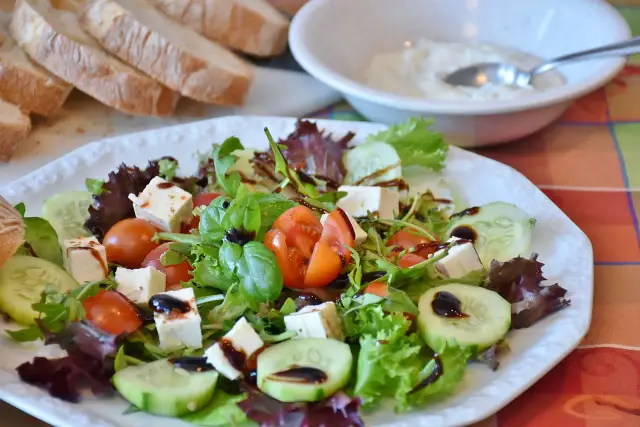 Świeża sałatka z pomidorami, ogórkiem i serem feta, polana aromatycznym sosem truflowym. Obok kromki chleba i miseczka dipu.