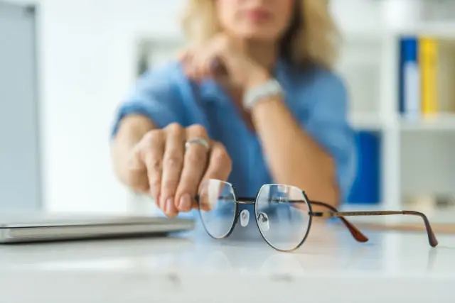 Kobieta w niebieskiej bluzce podaje okulary plusy do chodzenia.